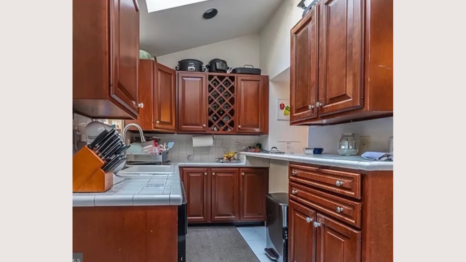 Existing kitchen sink wall with cherry uppers, a built-in wine rack and tile countertops